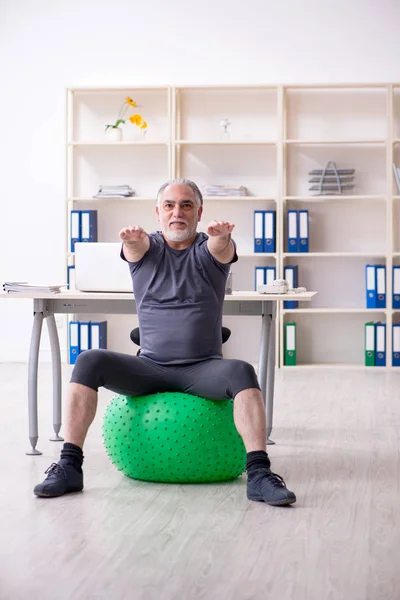 White bearded old man employee doing exercises in the office