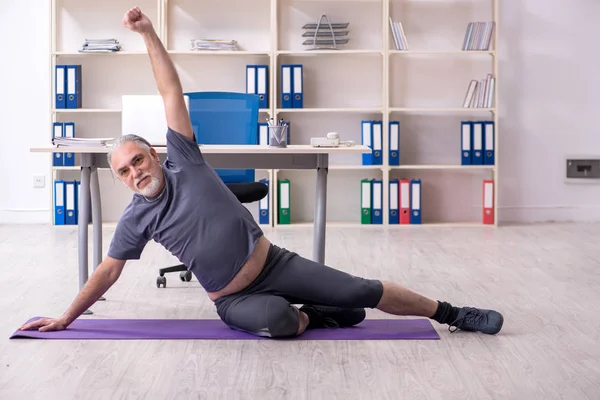 Vit skäggig gammal man anställd gör övningar på kontoret — Stockfoto