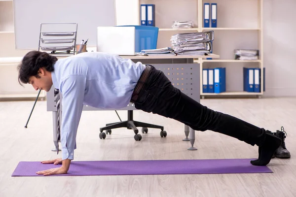 Young handsome male employee doing exercises in the office