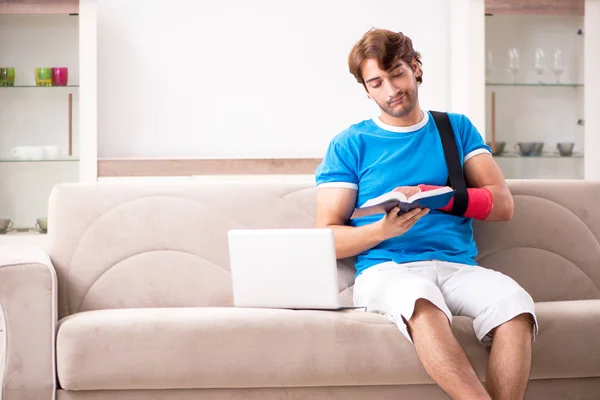 Ung man med skadad arm sitter på soffan — Stockfoto