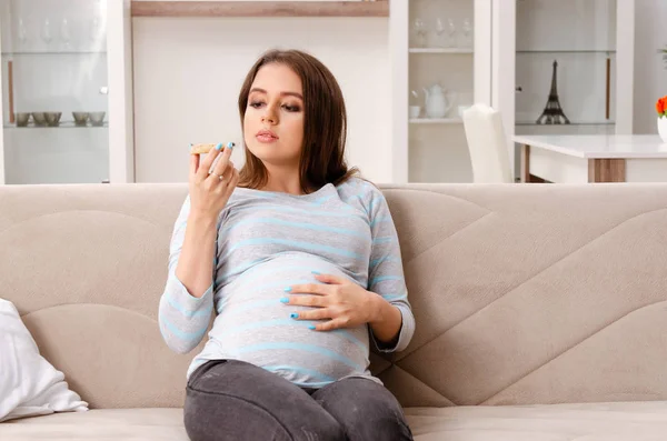 Mladá těhotná žena sedí na gauči doma — Stock fotografie