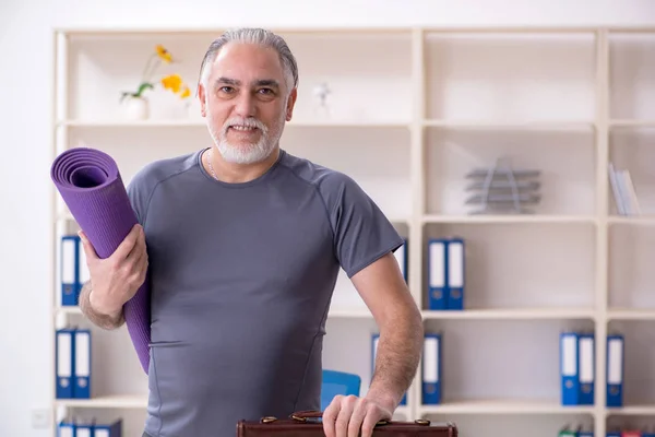 White bearded old man employee doing exercises in the office