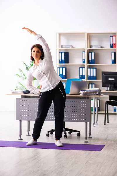 Medelålders kvinnlig anställd gör övningar på kontoret — Stockfoto
