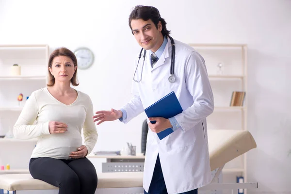 Vieille femme enceinte visitant jeune médecin masculin — Photo