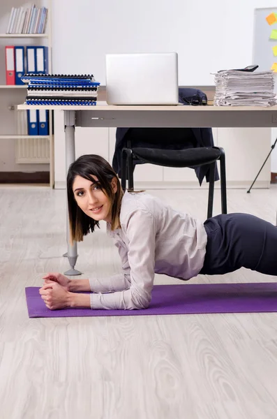 Jovem funcionária fazendo exercícios no local de trabalho — Fotografia de Stock