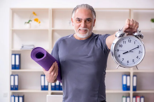 White bearded old man employee doing exercises in the office