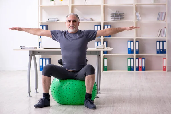 White bearded old man employee doing exercises in the office — Stock Photo, Image