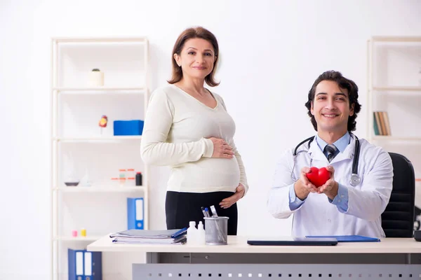 Vieja embarazada visitando joven médico masculino —  Fotos de Stock