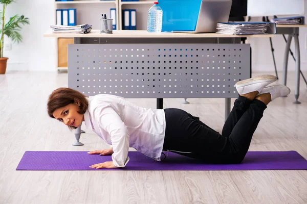 Empleada de mediana edad haciendo ejercicios en la oficina — Foto de Stock