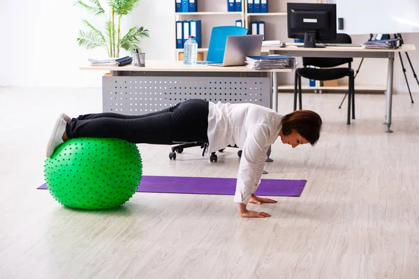 Middle-aged female employee doing exercises in the office — Stock Photo, Image