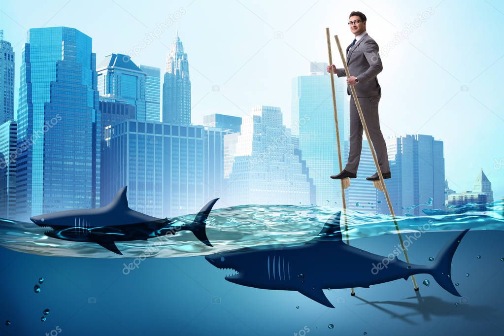Businessman walking on stilts among sharks