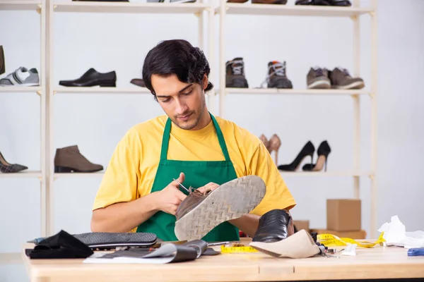 Молодой человек ремонтирует обувь в мастерской — стоковое фото