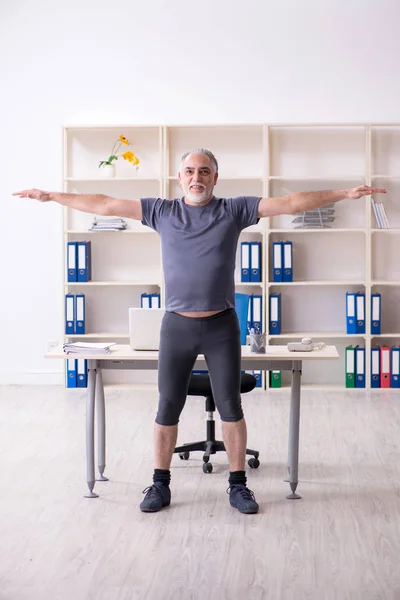 Белый бородатый старик работник делает упражнения в офисе — стоковое фото