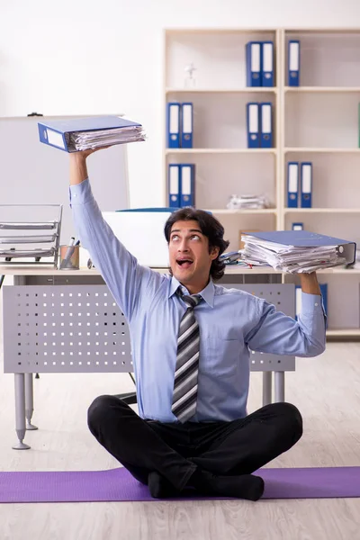 Young handsome male employee doing exercises in the office