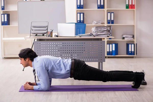 Joven empleado masculino guapo haciendo ejercicios en la oficina — Foto de Stock