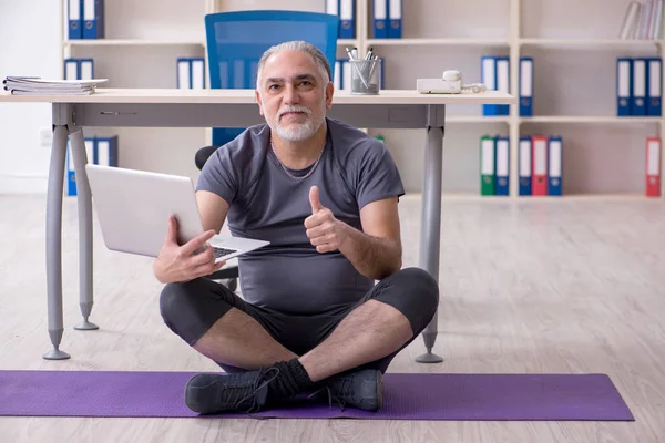 White bearded old man employee doing exercises in the office