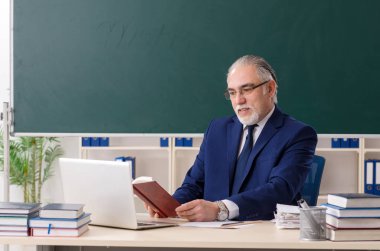 Tahtanın önünde yaşlı bir erkek öğretmen. 