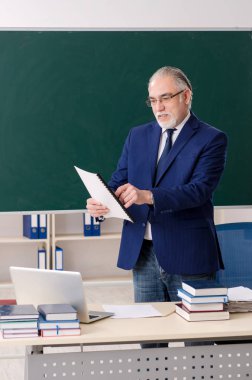 Tahtanın önünde yaşlı bir erkek öğretmen. 