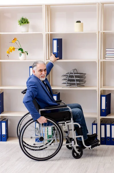 Aged employee in wheelchair working in the office — Stock Photo, Image