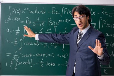 Young male math teacher in classroom  clipart