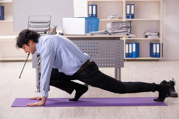 Young handsome male employee doing exercises in the office