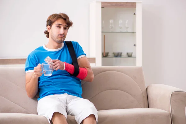 Joven con el brazo lesionado sentado en el sofá — Foto de Stock