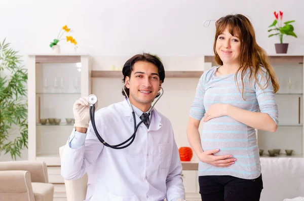 Jovem médico bonito visitando mulher grávida em casa — Fotografia de Stock
