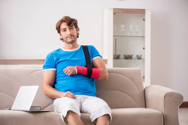 Jovem com o braço ferido sentado no sofá — Fotografia de Stock