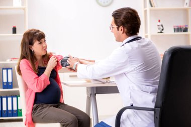 Hamile kadın doktoru ziyaret edip sağlıklı beslenmeyi tartışıyor.