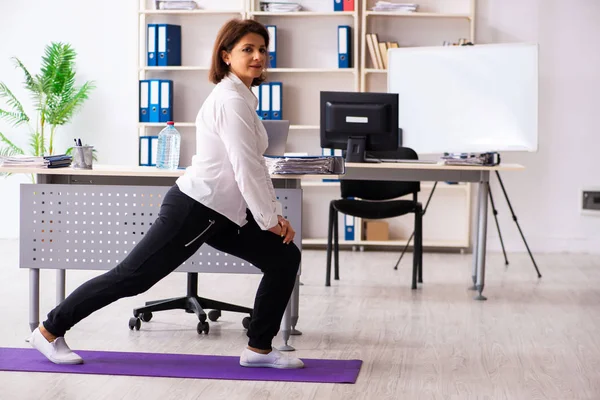 Empleada de mediana edad haciendo ejercicios en la oficina — Foto de Stock