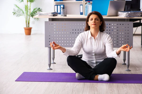 Middle-aged female employee doing exercises in the office