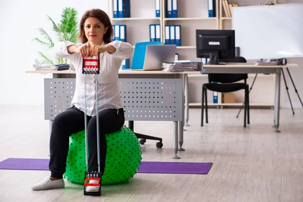 Mitarbeiterin mittleren Alters macht Übungen im Büro — Stockfoto