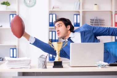 Young handsome businessman with rugby ball in the office clipart