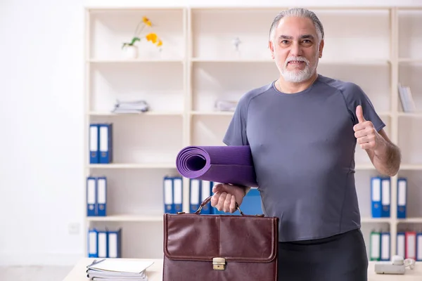 White bearded old man employee doing exercises in the office