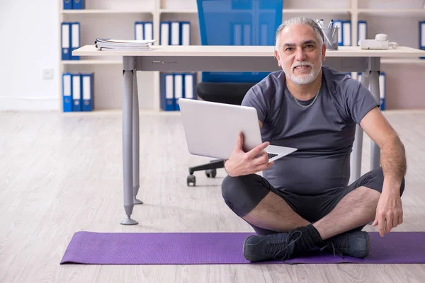 White bearded old man employee doing exercises in the office