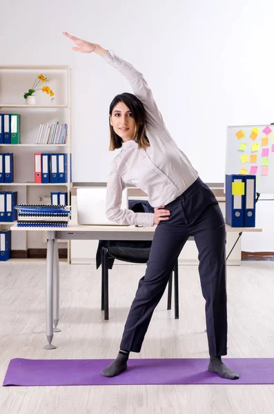 Joven empleada haciendo ejercicios en el lugar de trabajo — Foto de Stock