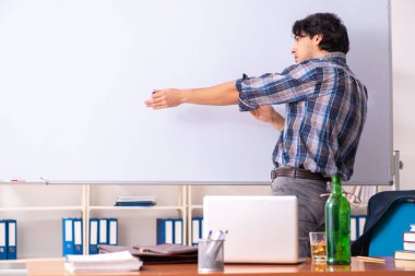 Erkek öğretmen sınıfta içiyor.