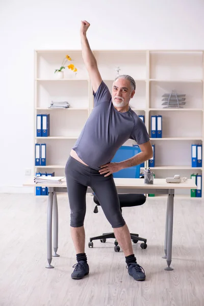 Bílá vousatý starý muž zaměstnanec dělat cvičení v kanceláři — Stock fotografie