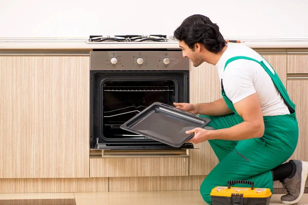 Jovem empreiteiro reparação forno na cozinha — Fotografia de Stock