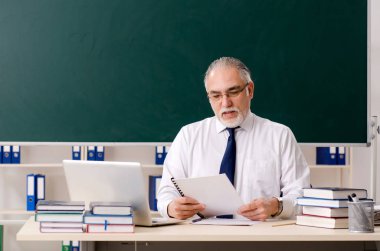 Tahtanın önünde yaşlı bir erkek öğretmen. 