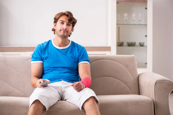 Νεαρός άνδρας με βραχίονα τραυματίες που κάθεται στον καναπέ — Φωτογραφία Αρχείου