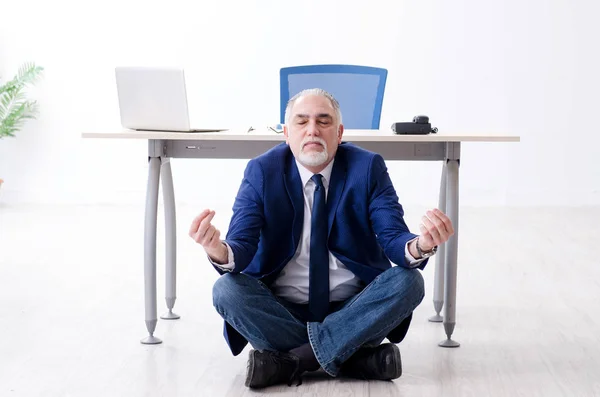 Aged businessman doing yoga exercises in the office — Stock Photo, Image