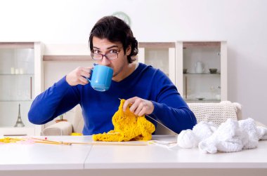 Genç yakışıklı adam evde örgü örüyor.