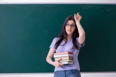 Genç bayan öğretmen yeşil panonun önünde. 