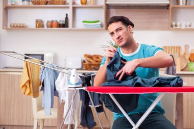 Genç adam evde çamaşır ütülüyor. 