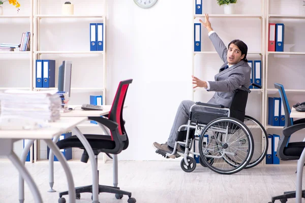 Young handsome employee in wheelchair working in the office