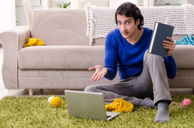 Genç yakışıklı adam evde örgü örüyor.