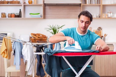 Genç adam evde çamaşır ütülüyor. 