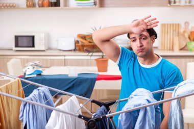 Genç adam evde çamaşır ütülüyor. 