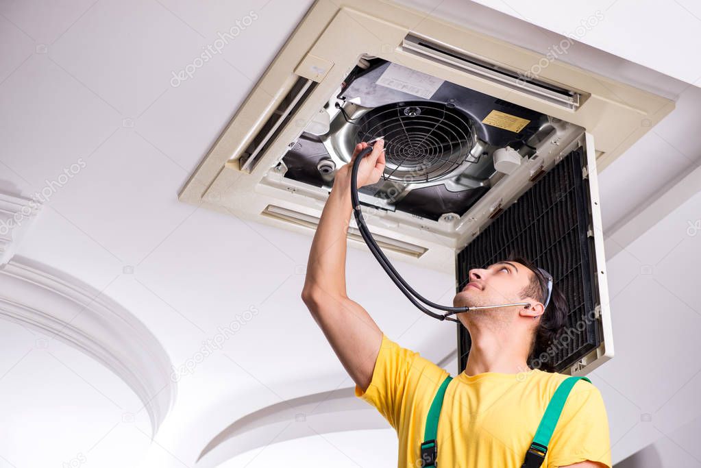 Young repairman repairing ceiling air conditioning unit 